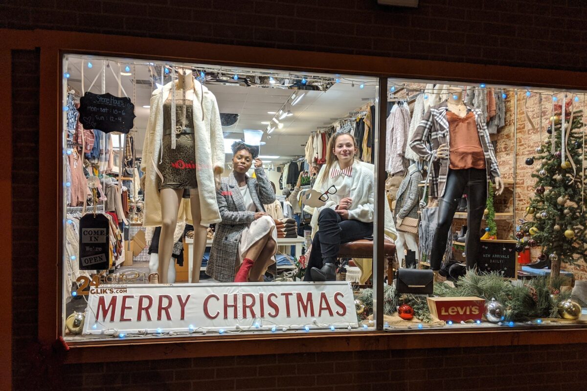 Two students in a clothing store window display done up for the Christmas holiday season.