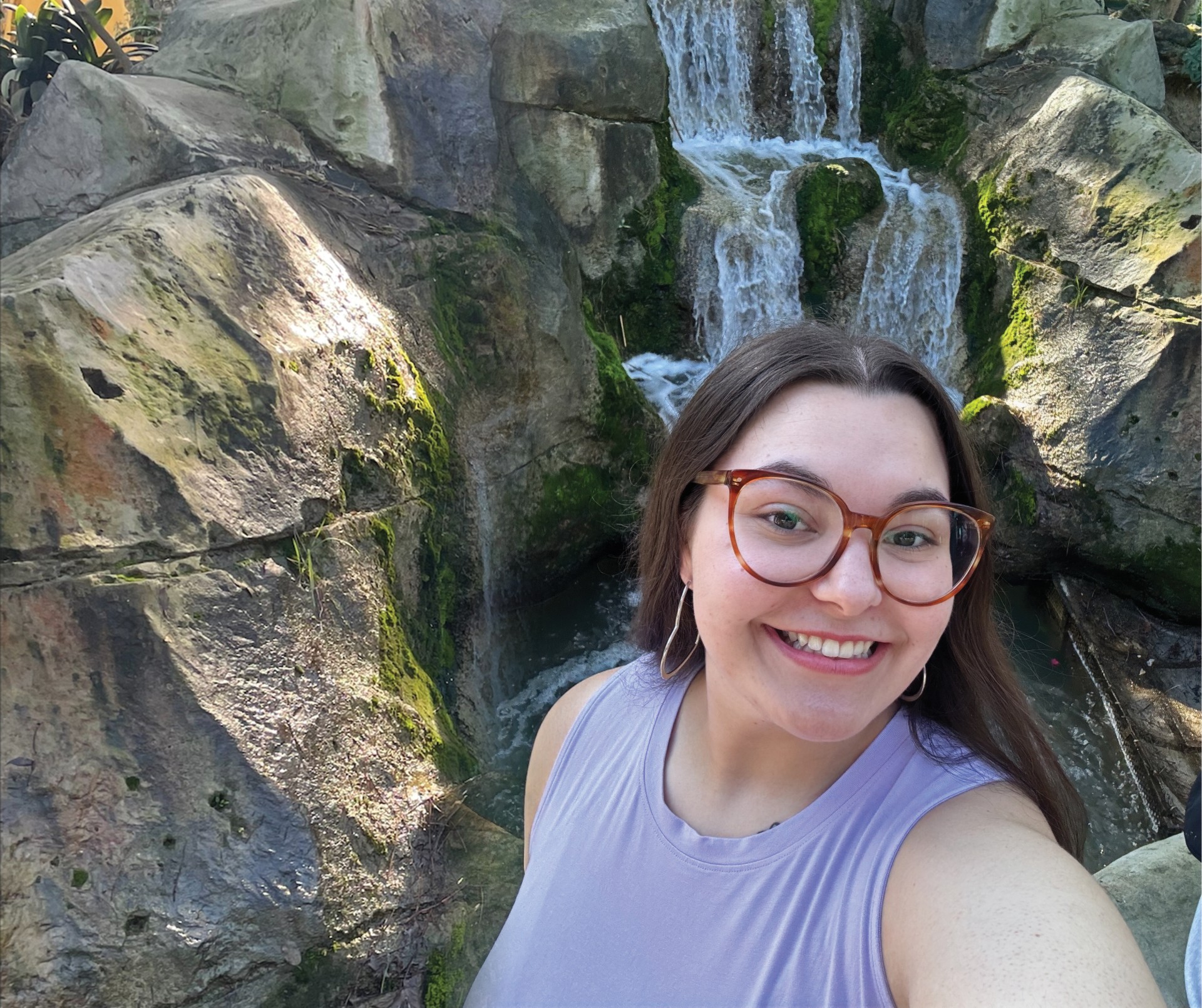 Smiling girl standing in front of a waterfall.