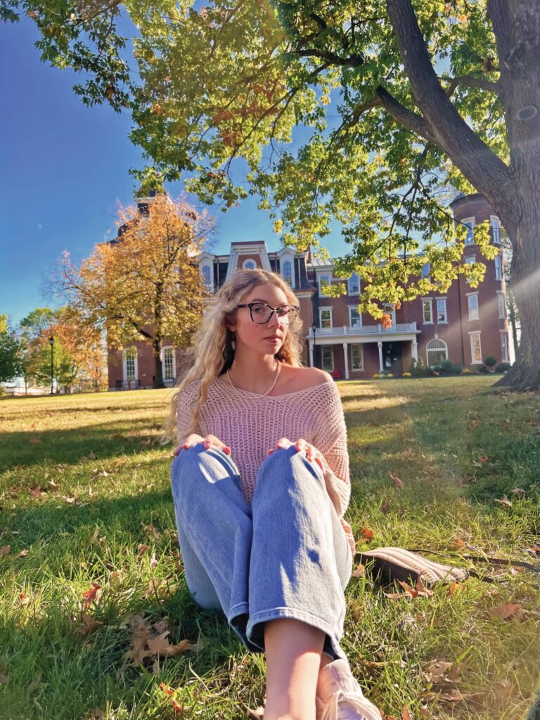 Girl sitting in the grass on the quad in front of Senior Hall