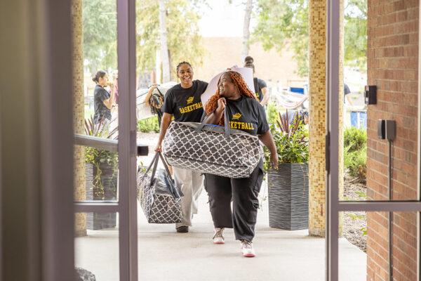 two students smiling while moving into their dorm room