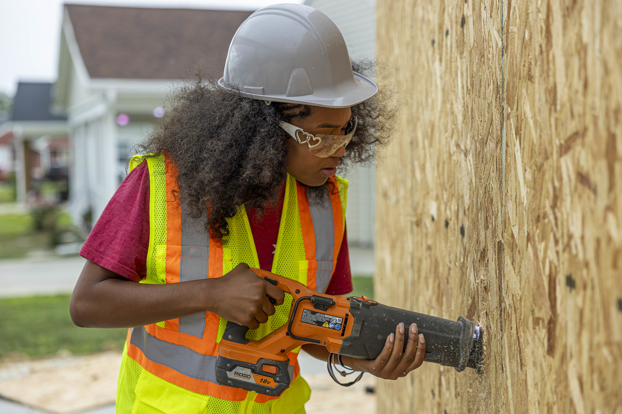 Student wearing hardhat uses tools to drill hole in wall.