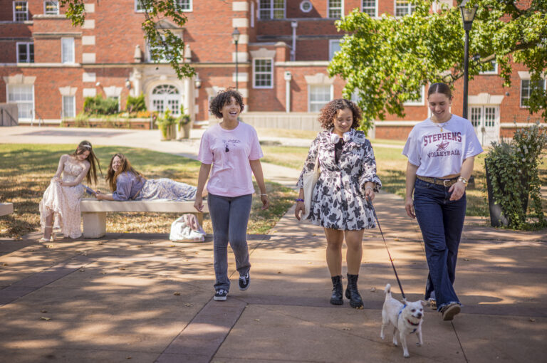three students walking a dog on campus during a summer day